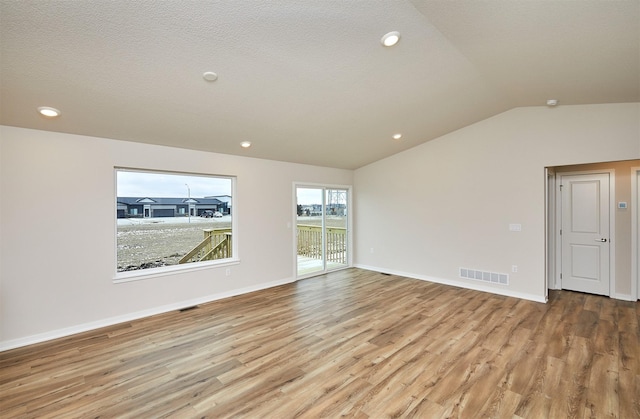 empty room with a textured ceiling, light wood-type flooring, and lofted ceiling