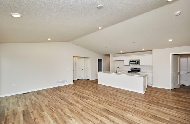 unfurnished living room featuring a textured ceiling, sink, vaulted ceiling, and light hardwood / wood-style flooring