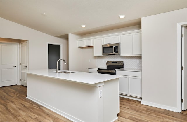 kitchen with tasteful backsplash, stainless steel appliances, sink, white cabinetry, and an island with sink