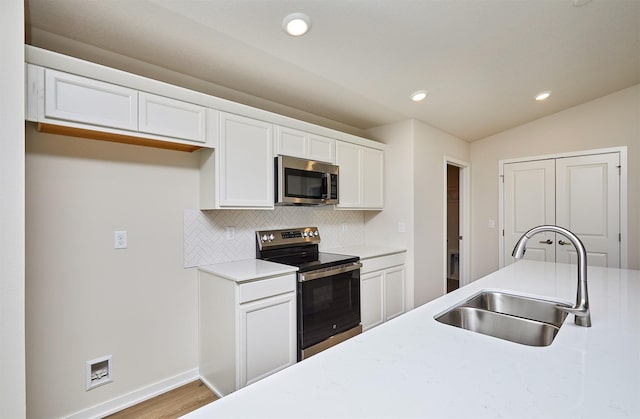 kitchen with backsplash, stainless steel appliances, vaulted ceiling, sink, and white cabinetry