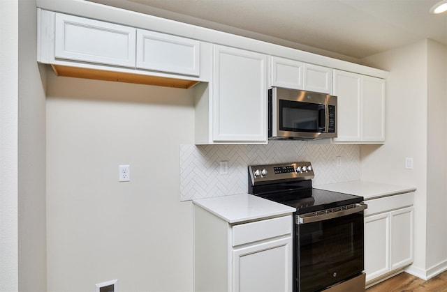 kitchen with white cabinets, appliances with stainless steel finishes, tasteful backsplash, and light hardwood / wood-style flooring