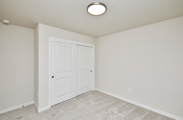 unfurnished bedroom featuring light carpet, a textured ceiling, and a closet