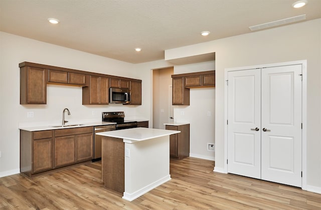 kitchen with stainless steel appliances, a center island, sink, and light hardwood / wood-style flooring