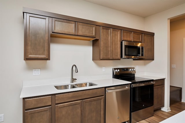 kitchen featuring dark brown cabinetry, sink, stainless steel appliances, and light wood-type flooring