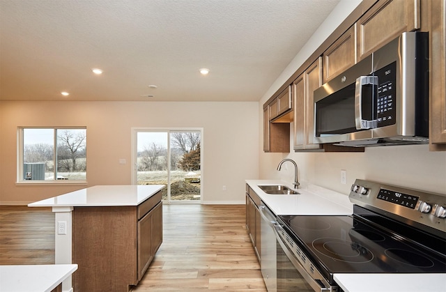 kitchen featuring sink, a center island, a textured ceiling, light wood-type flooring, and stainless steel appliances