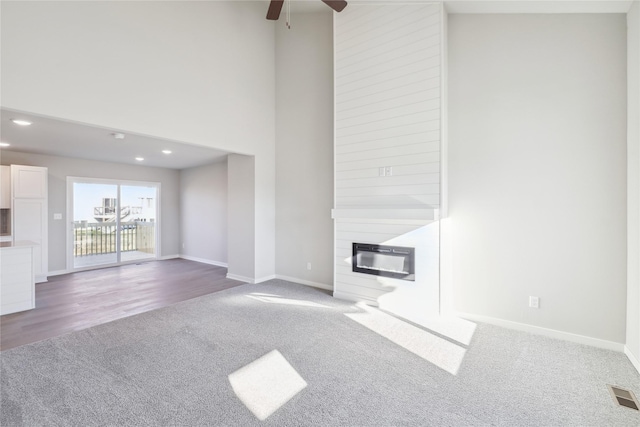 unfurnished living room featuring a towering ceiling, a large fireplace, hardwood / wood-style flooring, and ceiling fan