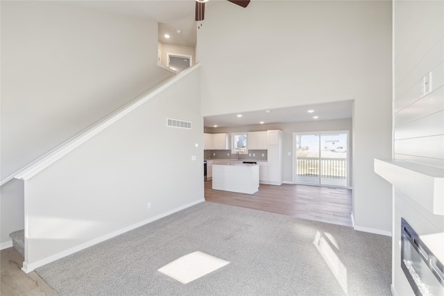 unfurnished living room featuring ceiling fan, a towering ceiling, and light wood-type flooring