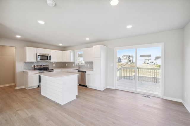 kitchen with stainless steel appliances, sink, a center island, light hardwood / wood-style floors, and white cabinetry