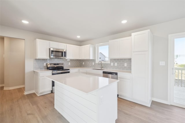 kitchen with sink, light wood-type flooring, appliances with stainless steel finishes, a kitchen island, and white cabinetry