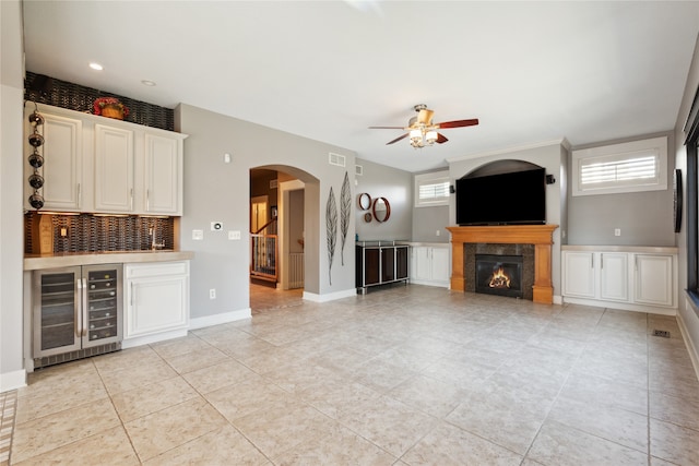 unfurnished living room with arched walkways, wine cooler, plenty of natural light, and baseboards