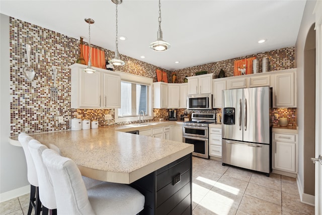 kitchen featuring decorative backsplash, a breakfast bar, decorative light fixtures, stainless steel appliances, and light countertops