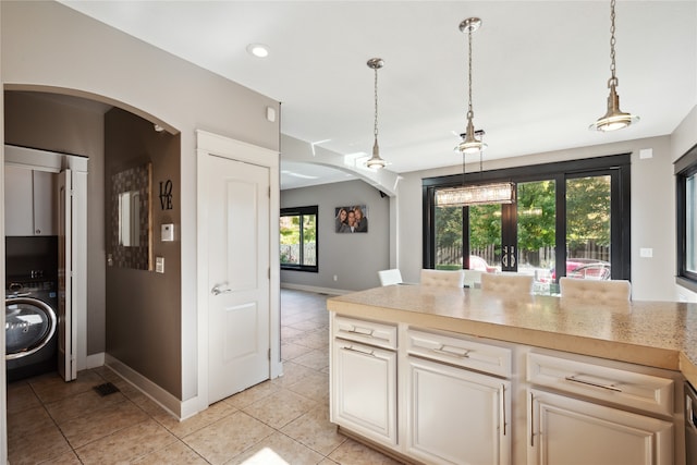 kitchen with baseboards, arched walkways, washer / clothes dryer, pendant lighting, and light tile patterned flooring