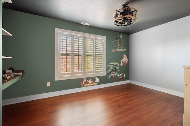 spare room with visible vents, a textured ceiling, baseboards, and wood finished floors