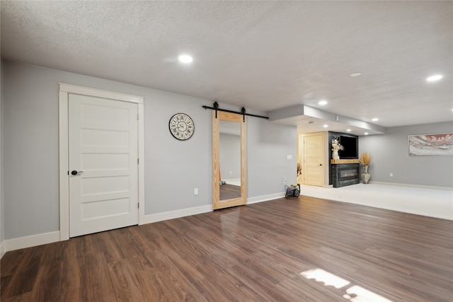 basement with a barn door, a glass covered fireplace, dark wood-style flooring, a textured ceiling, and recessed lighting