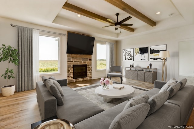 living room with beam ceiling, light hardwood / wood-style floors, ceiling fan, and a stone fireplace