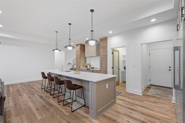 kitchen with pendant lighting, a kitchen bar, a kitchen island with sink, light brown cabinetry, and stainless steel stove