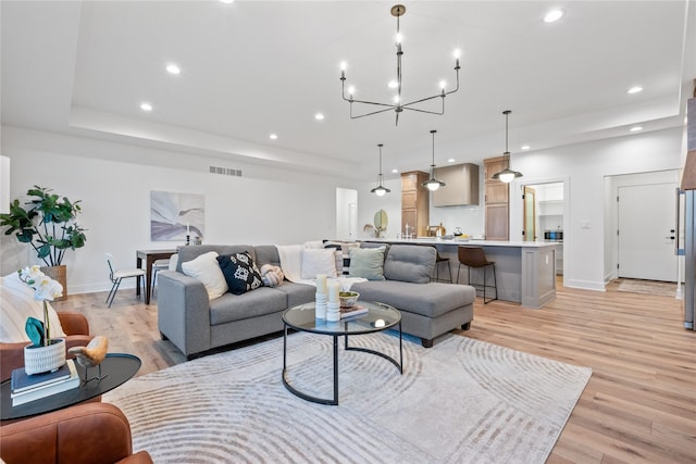 living room with light wood-type flooring, a tray ceiling, and an inviting chandelier