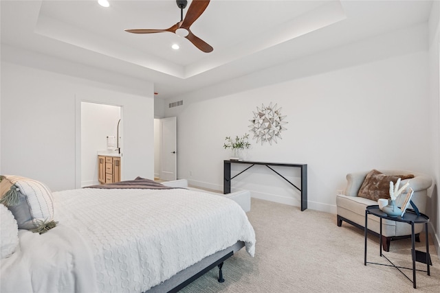 bedroom featuring light carpet, connected bathroom, a raised ceiling, and ceiling fan