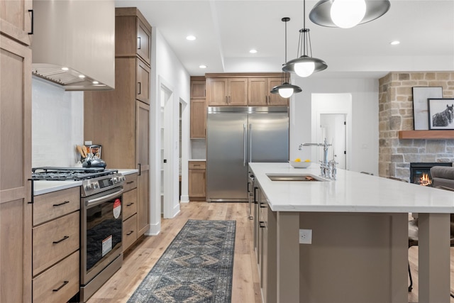 kitchen featuring sink, hanging light fixtures, a stone fireplace, an island with sink, and appliances with stainless steel finishes