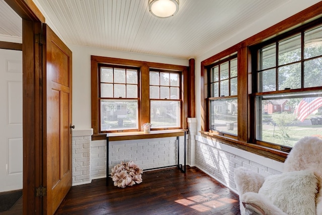 living area with brick wall, dark hardwood / wood-style flooring, and a healthy amount of sunlight