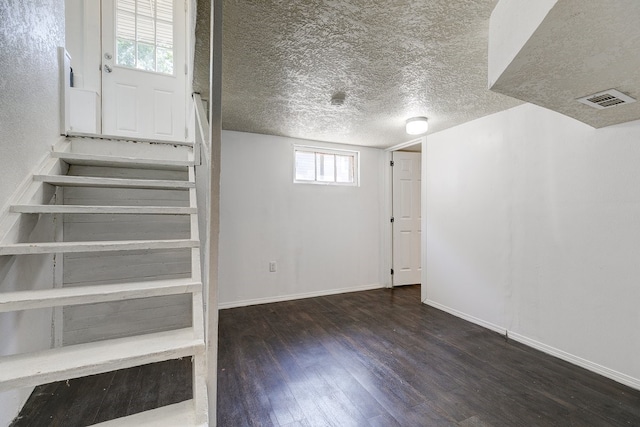 basement with dark wood-type flooring, a textured ceiling, and a healthy amount of sunlight