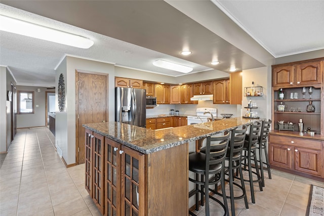 kitchen with stainless steel appliances, dark stone counters, kitchen peninsula, light tile patterned flooring, and a breakfast bar area