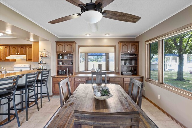 tiled dining area with ceiling fan and ornamental molding