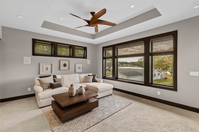 carpeted living room with a tray ceiling, plenty of natural light, and ceiling fan