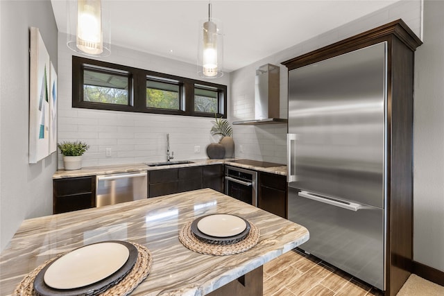 kitchen with wall chimney range hood, appliances with stainless steel finishes, hanging light fixtures, and sink