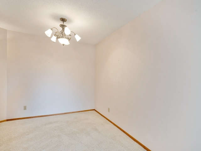 carpeted spare room with an inviting chandelier and a textured ceiling