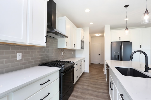 kitchen featuring sink, white cabinets, wall chimney range hood, black range with gas cooktop, and stainless steel fridge