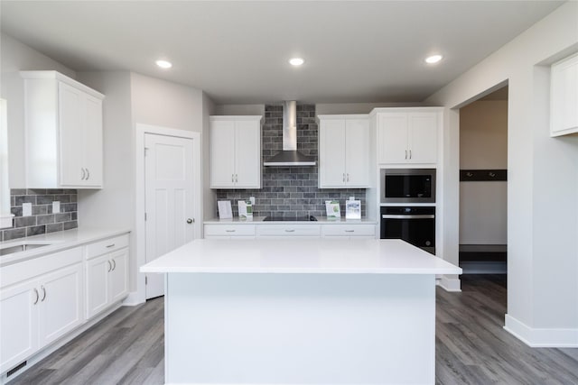 kitchen featuring white cabinets, wall chimney exhaust hood, a center island, and black appliances