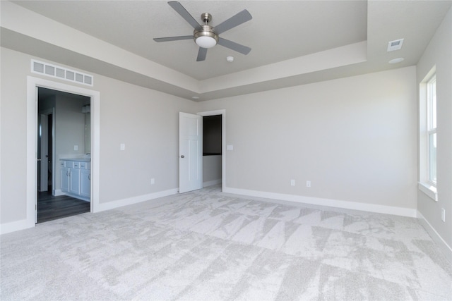 unfurnished bedroom with ensuite bath, light colored carpet, ceiling fan, and a tray ceiling