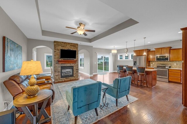 living room with hardwood / wood-style flooring, ceiling fan with notable chandelier, a raised ceiling, and a fireplace