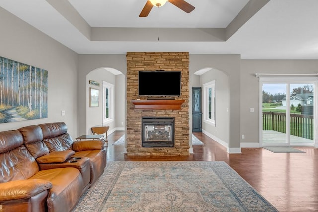 living room featuring a fireplace, a raised ceiling, ceiling fan, wood finished floors, and baseboards