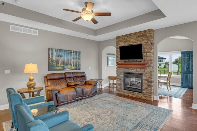 living room featuring baseboards, visible vents, a raised ceiling, wood finished floors, and a fireplace