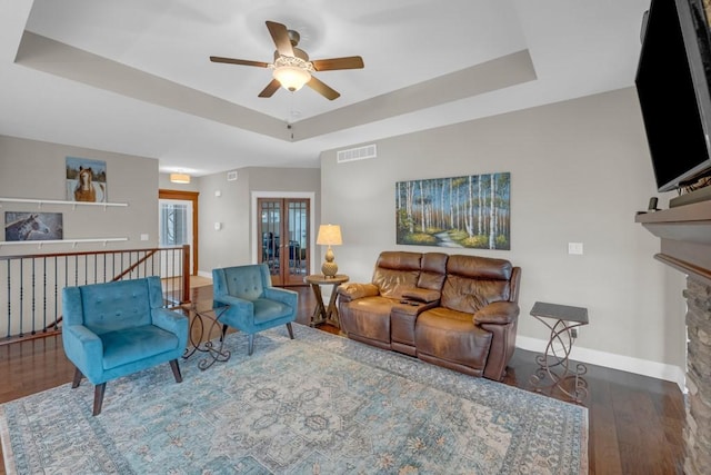 living room with a tray ceiling, visible vents, a stone fireplace, wood finished floors, and baseboards