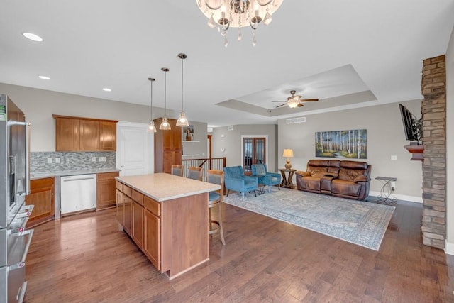 kitchen with dishwashing machine, a tray ceiling, light wood finished floors, and backsplash