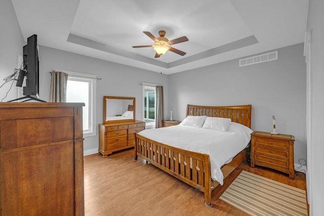 bedroom with a tray ceiling, visible vents, a ceiling fan, light wood-type flooring, and baseboards