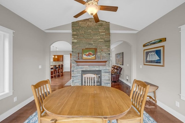 dining space featuring baseboards, arched walkways, wood finished floors, vaulted ceiling, and a fireplace