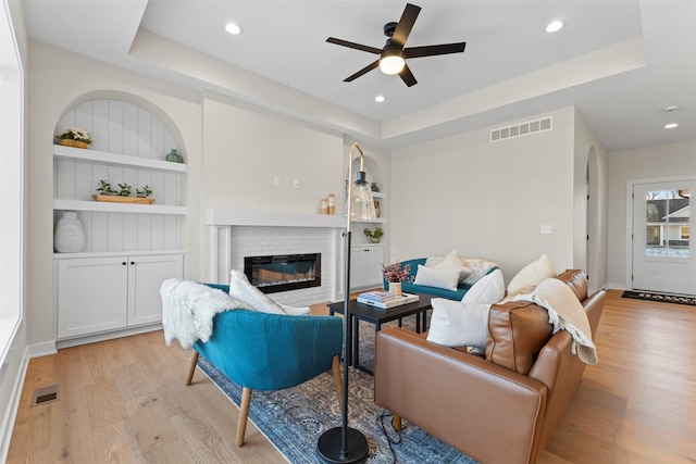 living room featuring a raised ceiling, a fireplace, light wood-type flooring, and built in features