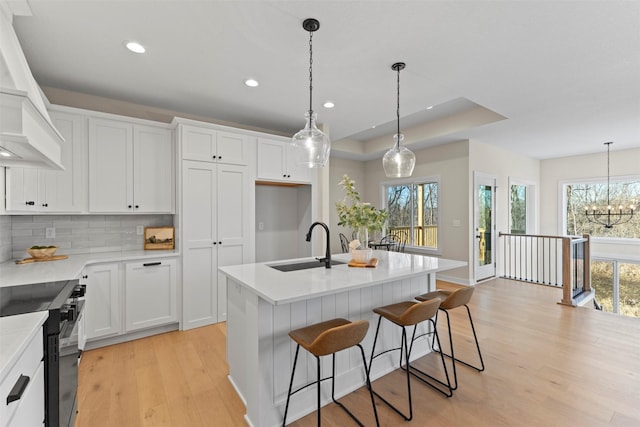 kitchen with hanging light fixtures, a center island with sink, decorative backsplash, an inviting chandelier, and white cabinets