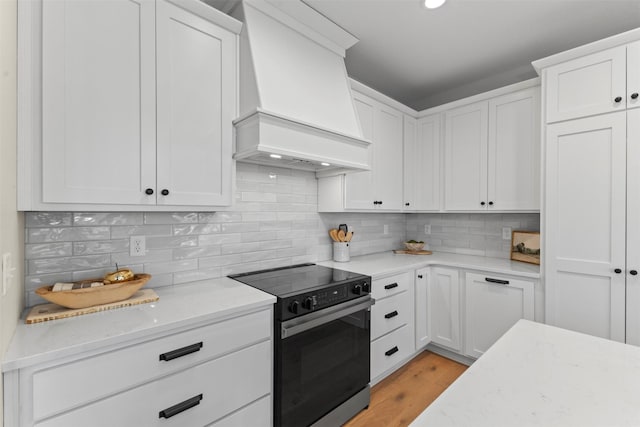 kitchen featuring light stone counters, range with electric stovetop, custom range hood, and white cabinetry