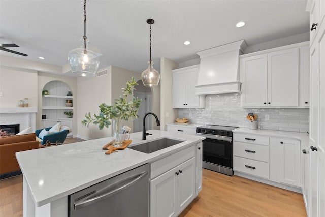 kitchen featuring a center island with sink, stainless steel appliances, premium range hood, white cabinets, and sink