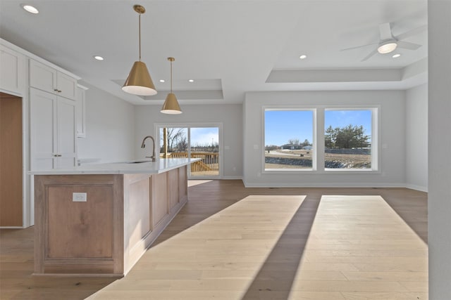 kitchen with white cabinetry, a raised ceiling, pendant lighting, dark hardwood / wood-style flooring, and a kitchen island with sink