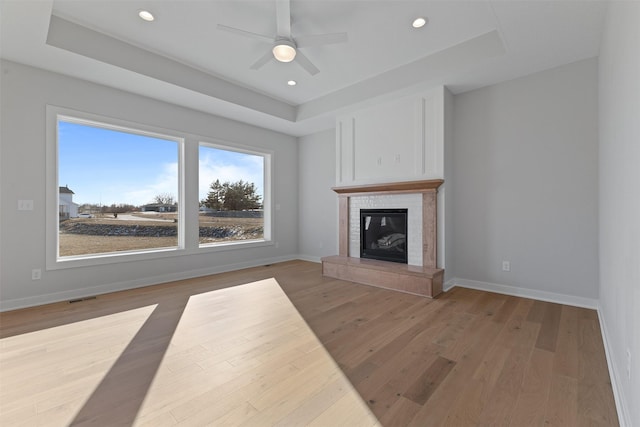 unfurnished living room featuring a raised ceiling, ceiling fan, and hardwood / wood-style floors