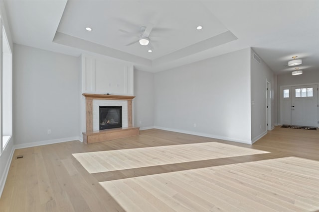 unfurnished living room with a raised ceiling, ceiling fan, and light wood-type flooring