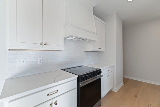 kitchen with premium range hood, black / electric stove, tasteful backsplash, light wood-type flooring, and white cabinets