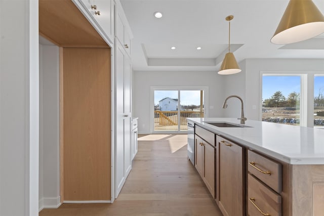 kitchen featuring decorative light fixtures, a center island with sink, a raised ceiling, white cabinetry, and sink