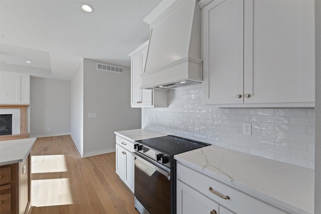 kitchen featuring stainless steel electric stove, custom exhaust hood, and white cabinets